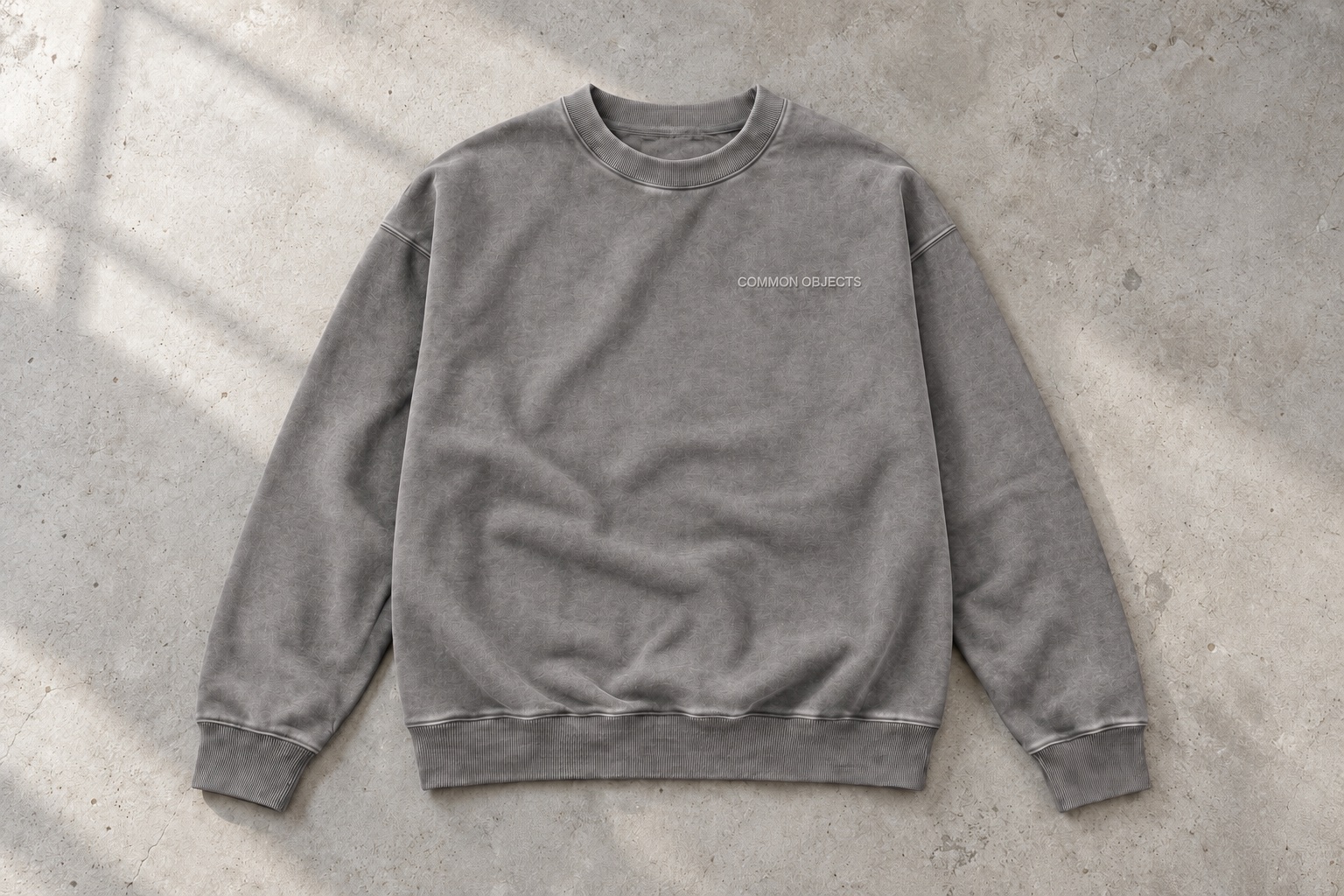 Stone gray crewneck with tonal Common Objects chest embroidery on concrete