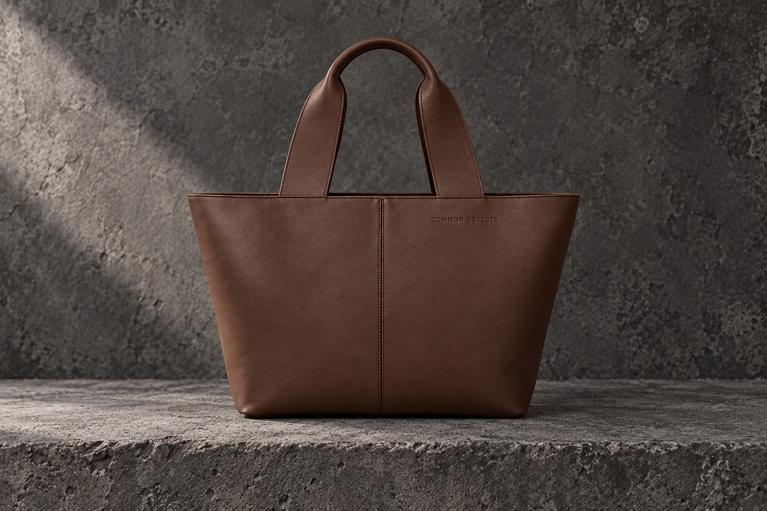 Brown leather Common Objects tote on dark gray concrete